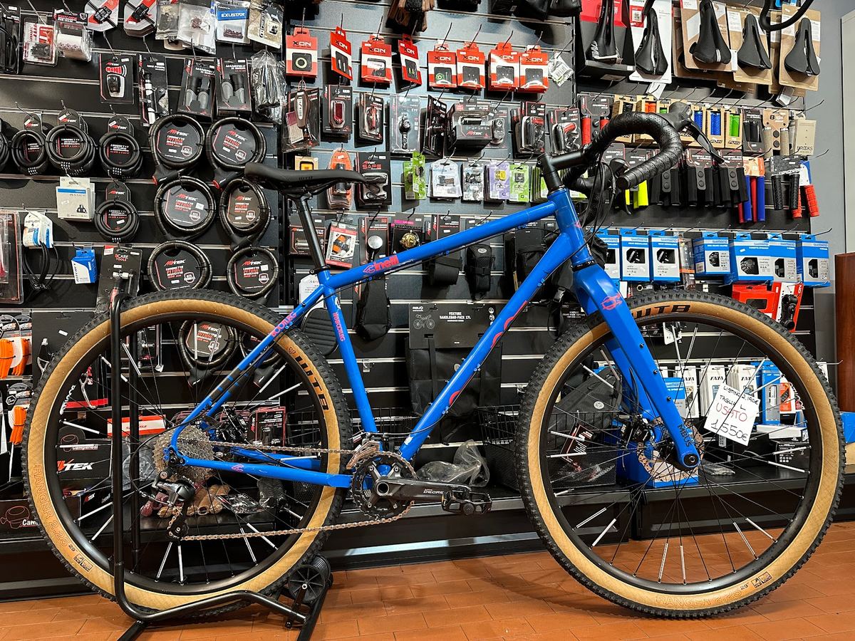 Bici gravel blu con copertoni color para, sul cavalletto in negozio