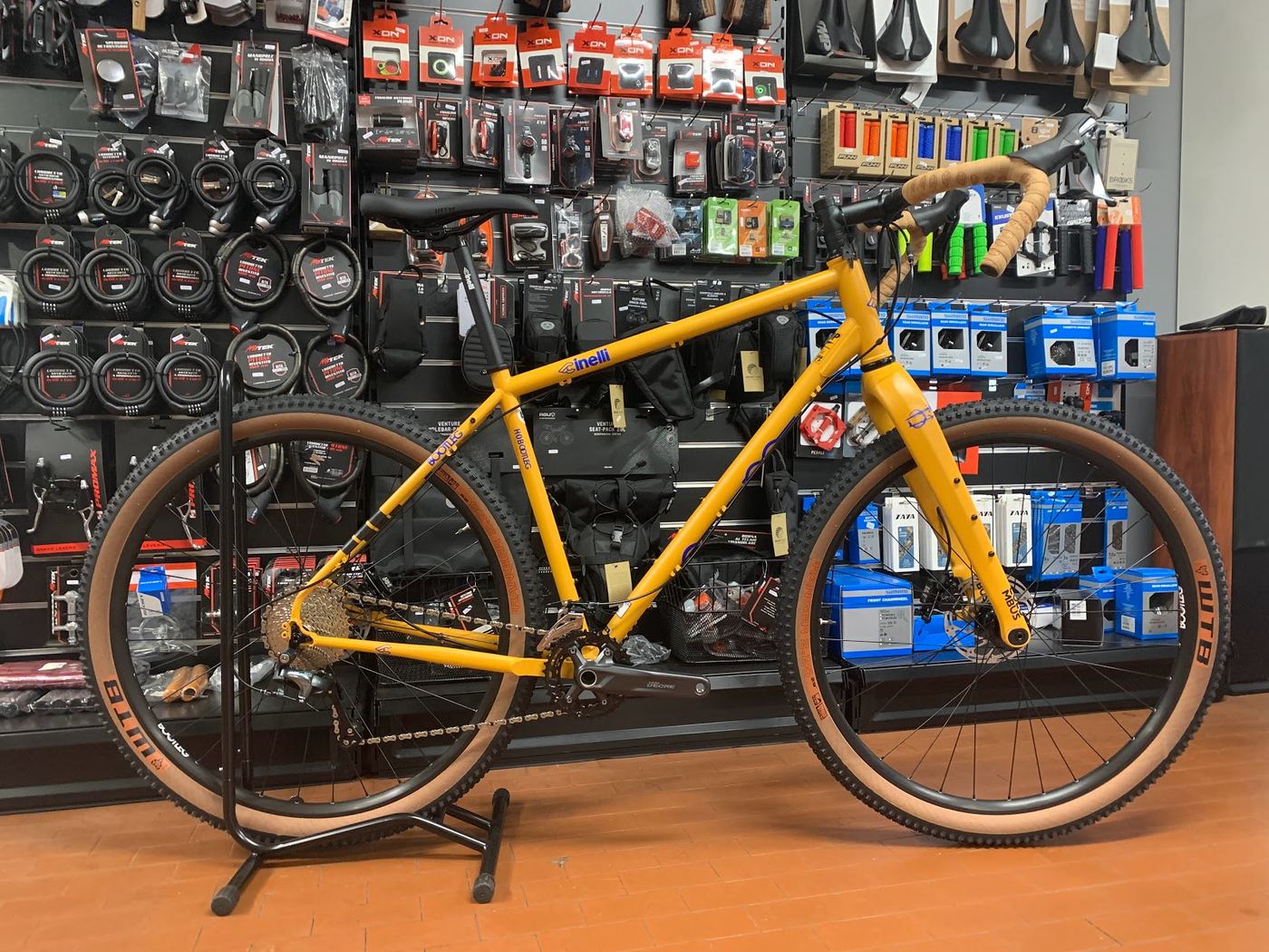 Bici gravel Cinelli Hobootleg gialla con copertoni tassellati, davanti alla parete dei ricambi