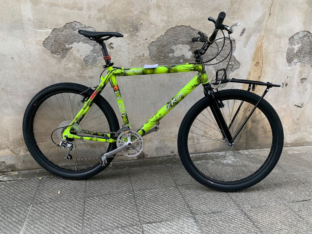 Mountain bike con telaio verde fluo mimetico e portapacchi, appoggiata a un muro